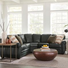 a living room with a sectional couch and coffee table in front of two large windows