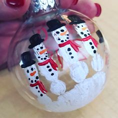 a hand holding a glass ornament with snowmen on it