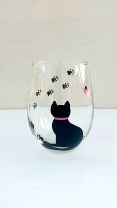 a wine glass with a black cat on the bottom and paw prints in pink around it