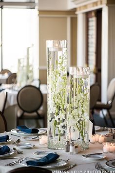 two tall vases filled with white flowers on top of a table covered in plates and silverware