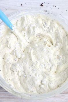 a bowl filled with white sauce sitting on top of a wooden table next to a blue spoon