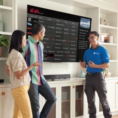 three people are standing in front of a large television screen and talking to each other