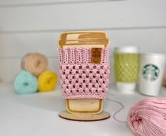 a knitted cup holder sitting on top of a table next to yarn and coffee mugs