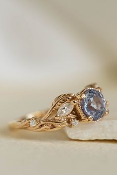 a gold ring with an oval blue topazte surrounded by leaves and diamond accents