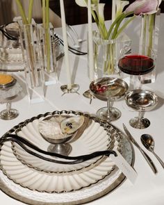 a white table topped with plates and silverware next to vases filled with flowers