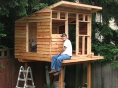 a man sitting on top of a wooden structure next to a tree house in the yard