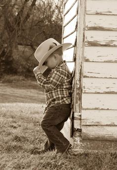 a young boy wearing a cowboy hat leaning against a barn