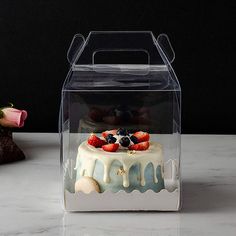 a cake in a clear box with fruit on top