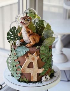 a cake decorated with animals and plants on top of a white table next to a window