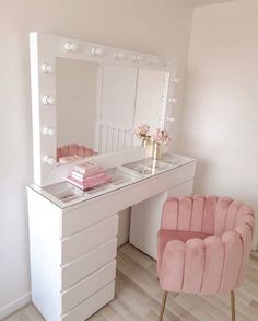 a pink chair sitting in front of a white vanity with lights on it and a mirror