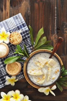 a bowl of oatmeal with banana slices and flowers on the side next to two spoons