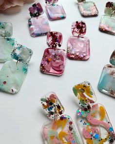 many different colored glass pieces are arranged on a white surface with flowers in the background