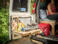 a woman is sitting in the back of a van with food and drinks on it