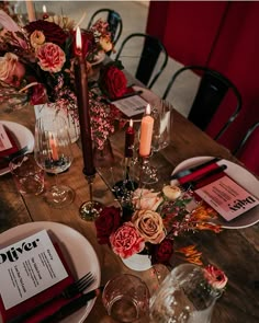 a wooden table topped with plates and glasses filled with flowers, candles and menus