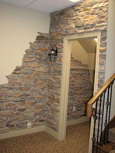 an open door leading to a room with stone walls and stairs in the corner, next to a set of wooden banisters