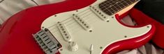 a red and white electric guitar sitting on top of a bed