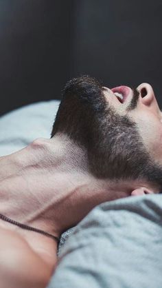 a man laying on top of a bed with his eyes closed and head tilted to the side