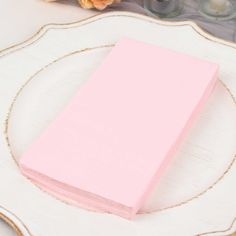 a stack of pink napkins sitting on top of a white plate next to flowers