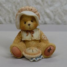 a brown teddy bear wearing a white hat and holding a pie