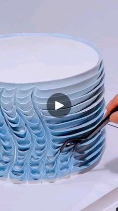 a person is cutting paper with scissors on top of a stack of blue plates that are stacked together