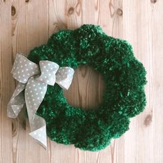 a green wreath with white polka dots and a gray bow on the front is sitting on a wooden surface