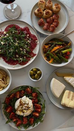 a table topped with plates and bowls filled with food next to wine glasses on top of a white table cloth