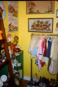 a room with yellow walls and various children's clothing hanging on the rack in front of it