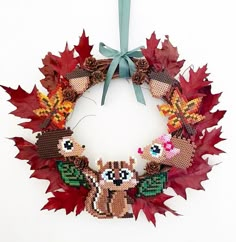 a cross stitch fall wreath hanging on a wall with leaves and acorns around it