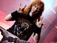 a man with long hair and glasses holding a guitar in front of him on stage