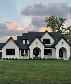 a large white house sitting on top of a lush green field under a cloudy sky