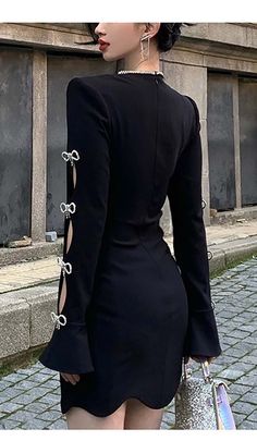 a woman wearing a black dress with long sleeves and laces on the back, standing in