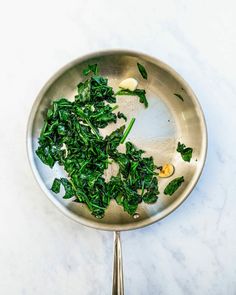 spinach and eggs in a pan on a marble counter top with spoons next to it