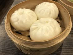 three dumplings in a wooden bowl with chopsticks next to them on a table