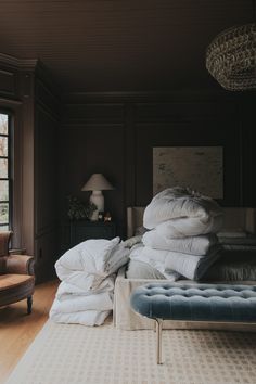 a room with a bed, chair and pillows on the floor in front of a window