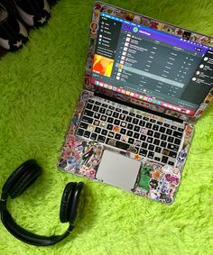 an open laptop computer sitting on top of a green rug next to headphones and a pair of black earbuds