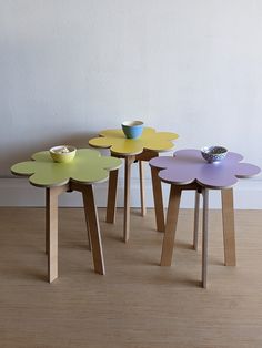 three small tables with flower designs on each side and a bowl in the middle, against a white wall