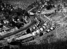 black and white photograph of an aerial view of houses on a hill with mountains in the background