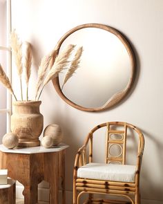 a round mirror hanging on the wall next to a table with a chair and potted plant