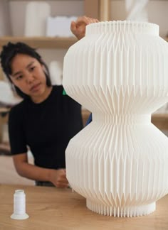 a woman sitting at a table next to a white vase on top of a wooden table