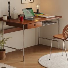 a laptop computer sitting on top of a wooden desk next to a chair and potted plant