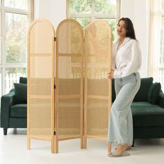 a woman standing next to a room divider in front of a couch and window