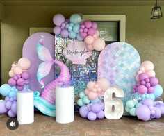 balloons, candles and decorations are displayed on the floor in front of a wall with a mermaid theme