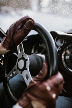 the driver's hand on the steering wheel of a car with rain coming down