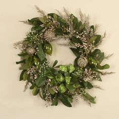 a wreath with green leaves and silver berries on the front is hung on a wall