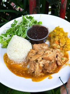 a white plate topped with meat, rice and veggies next to sauce on top of it