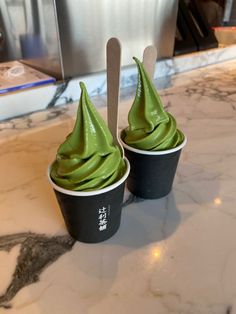 two cupcakes with green frosting in front of a counter top and a spoon