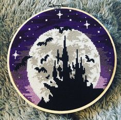 a cross stitched picture of a castle in the night sky with bats flying over it