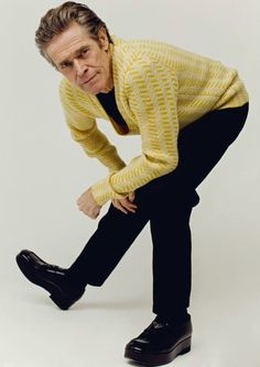 a man in a yellow sweater and black pants poses with his hands on his hips