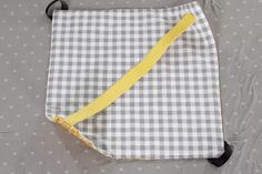 a gray and white checkered bag with yellow straps on the front, sitting on a bed