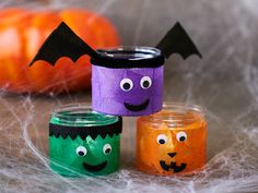 three halloween jars with faces and bats painted on them sitting next to some pumpkins